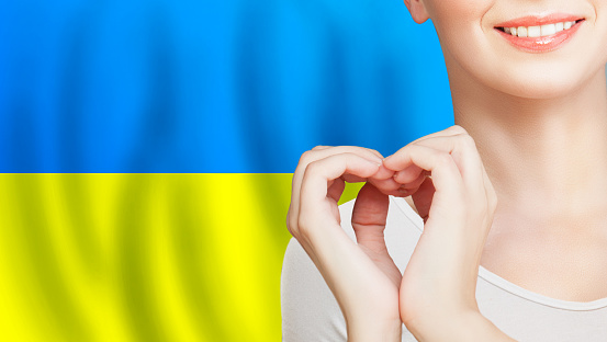 Love and help Ukraine concept. Woman making heart sign on Ukrainian flag background