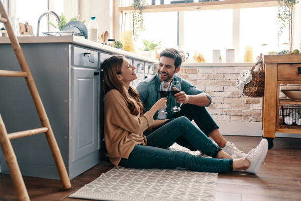 Love is in the air. Beautiful young couple drinking wine while sitting on the kitchen floor at home flirting photos stock pictures, royalty-free photos & images