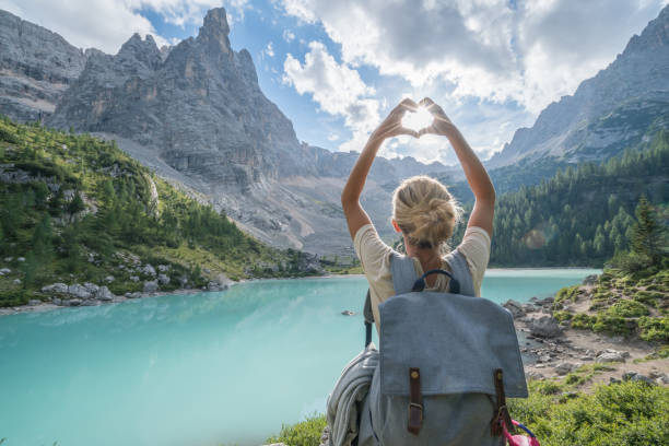 Young woman making heart shape finger frame on Alpine lake in Alto Adige region, Italy.