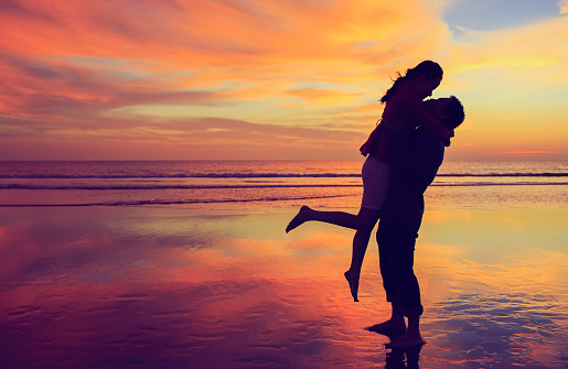 Happy young couple kissing and hugging each other in sunset background