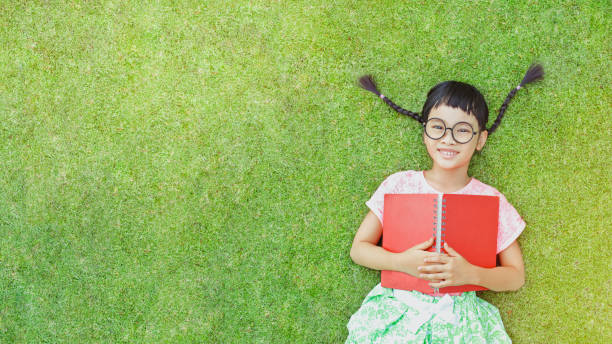 Love to read Little girl lay on grass and reading a book in a summer day chinese girl hairstyle stock pictures, royalty-free photos & images