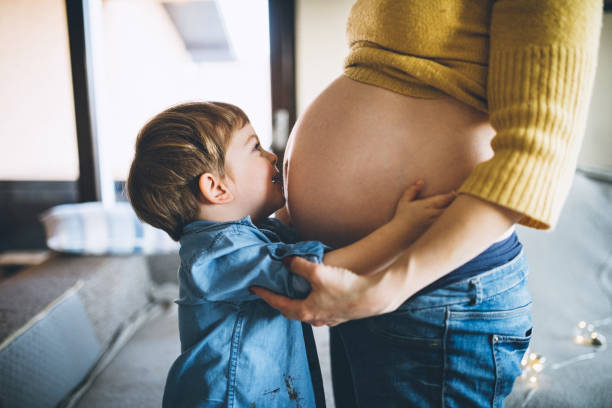 I love you already, baby Little boy kissing his pregnant mothers belly human abdomen stock pictures, royalty-free photos & images