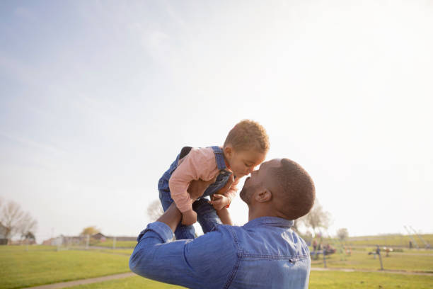 I Love You Dad A black mid adult man and his toddler son wearing casual clothing in a public park. They are sharing a cute moment while the father holds his son up on a sunny day in spring. fathers day stock pictures, royalty-free photos & images