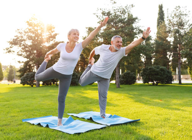 Lovely active fit elderly family couple practicing partner yoga outside in nature standing on mats stock photo