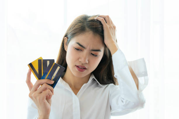 A lovely Asian woman holding three credit cards, she is so distressed by her debts that she cannot solve it. stock photo