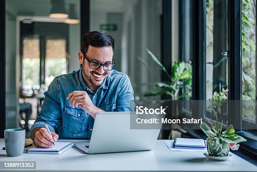 istock Lovely business man, attending a meeting online, writing stuff down. 1388913352
