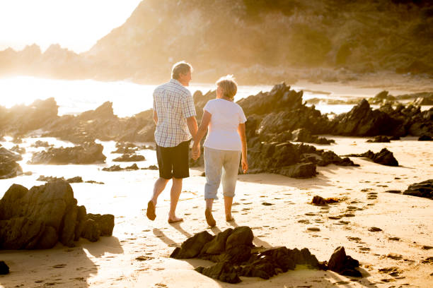 lovely senior mature couple on their 60s or 70s retired walking happy and relaxed on beach sea shore in romantic aging together and retirement husband and wife lifestyle concept stock photo