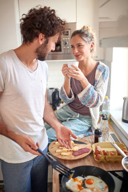 lovely young couple making breakfast, drinking coffee, talking in the kitchen, smiling stock photo