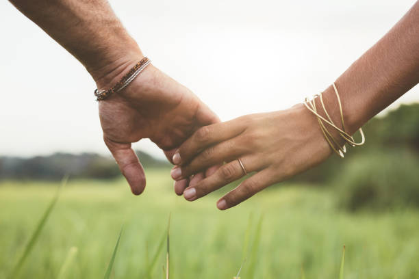 Loving couple holding hands in a field Horizontal shot of young couple walking through meadow holding hands with focus on hands . holding hands stock pictures, royalty-free photos & images