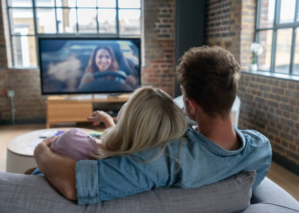 Loving couple watching television at home Portrait of a loving couple watching television at home sitting on the sofa - lifestyle concepts. **PICTURE ON SCREEN BELONGS TO US** watching tv stock pictures, royalty-free photos & images