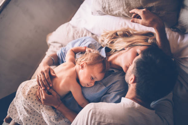 Loving couple with sleeping baby kissing in bed stock photo