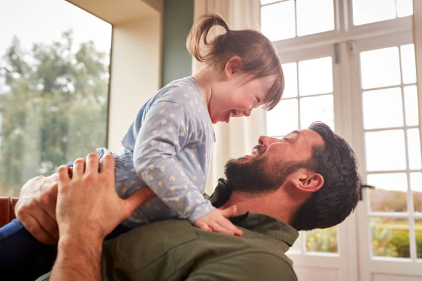 Loving Father Playing With Laughing Down Syndrome Daughter At Home Together stock photo