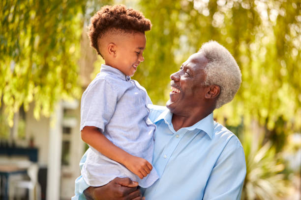 Loving Grandfather Holding Grandson In Arms In Garden At Home stock photo