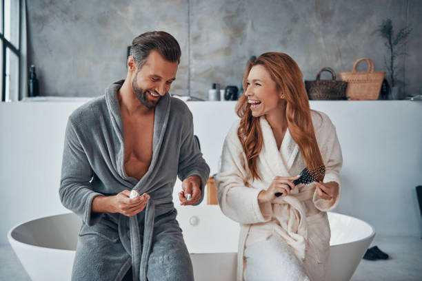 Loving young couple in bathrobes smiling and cleaning teeth stock photo