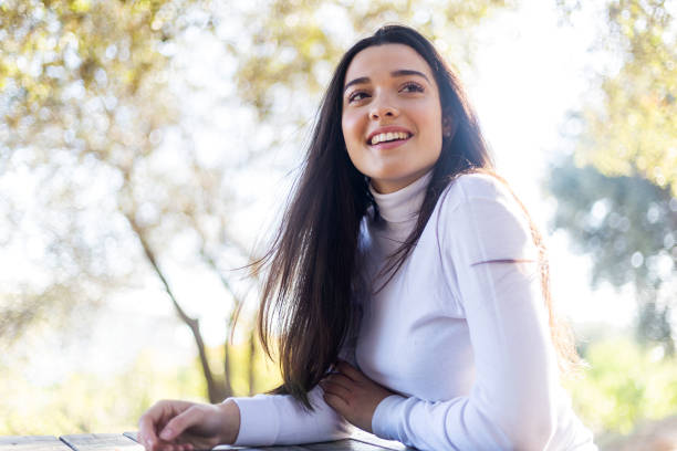 Low angle portrait of a smiling beautiful young hispanic woman sitting on park while looking camera Low angle view of a smiling beautiful young hispanic woman sitting on park while looking camera beautiful latina woman stock pictures, royalty-free photos & images