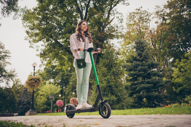 Low angle view full body photo of pretty happy positive curly hair girl ride electric scooter in park fun enjoy stock photo