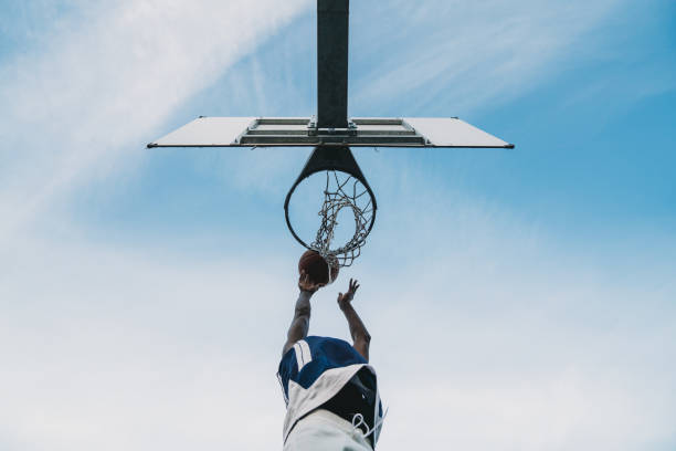 Low angle view of a young adult man scoring a goal in a basketball court stock photo