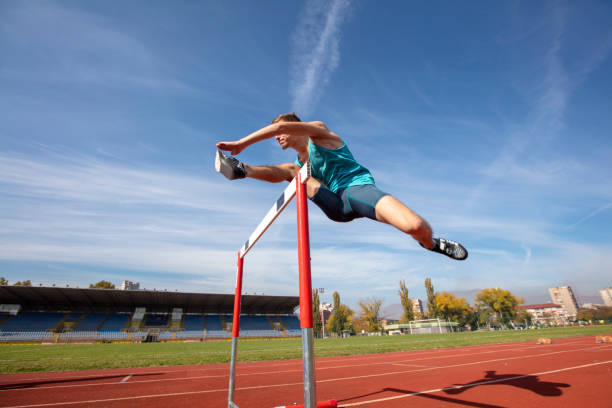 Low angle view of determined male athlete jumping over a hurdles stock photo
