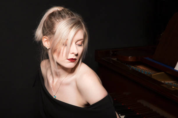 Low key blonde girl sat at a vintage grand piano stock photo