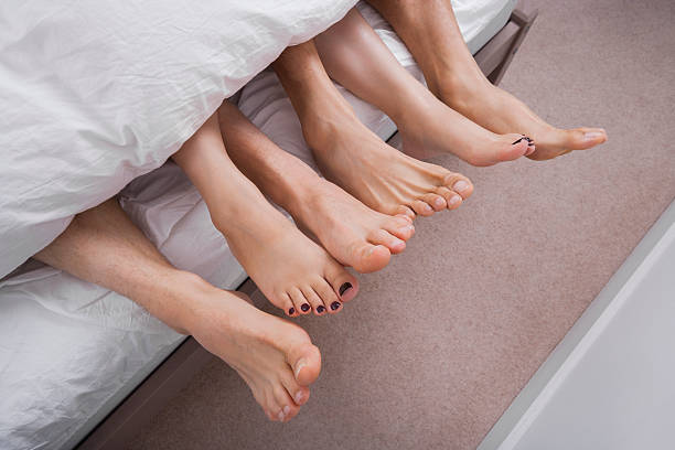 Low section of woman with two men in bed stock photo