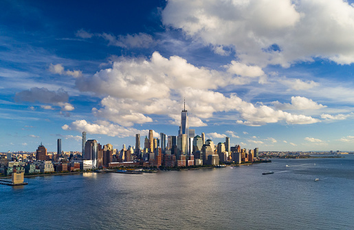 Lower Manhattan (Downtown New York City) elevated skyline view during the late afternoon with the Hudson River in the foreground and a deep blue sky with puffy cumulus clouds in the background.