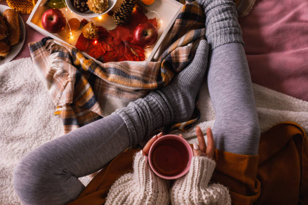 Lower section of unrecognizable woman enjoying a cup of tea Directly above shot of unrecognizable young woman sitting in her cozy bed and enjoying a warm cup of tea on a cold autumn day. hygge stock pictures, royalty-free photos & images