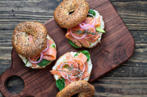 Lox - Everything bagel with smoked salmon, spinach, red onions, avocado and cream cheese Lox - Everything bagel with smoked salmon, spinach, red onions, avocado and cream cheese over a rustic wood table background. Image shot from top view or flat lay position. smoked salmon photos stock pictures, royalty-free photos & images