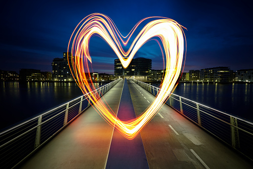 Glowing heart painted with light in the middle of the night. The heart is located in the middle of a bridge in an urban area in a big city / capital