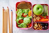 Lunch box with salad and healthy food prepared for school. Flat lay with color pencils on marble background