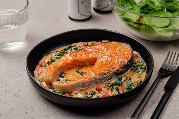 Lunch with creamy garlic butter salmon steak and salad. Pan seared salmon in a creamy sauce with spinach and sun dried tomatoes. stock photo