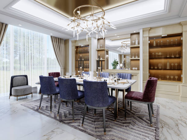 Luxurious dining area in a modern interior with a white table and burgundy and blue upholstered chairs near the shelves with glassware for serving. stock photo