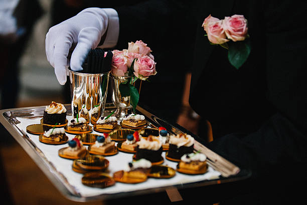 白い手袋を持つプロのケータリングは、カクテルの結婚式のパーティーやイベントケータリング中にフィンガーデザートの食べ物を提供しています。