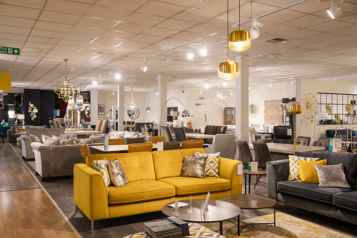 A wide angle of a furniture store with no people in. There is various different sofas and lamps and furniture on the shop floor for display purposes.
