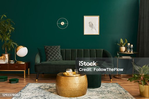 istock Luxury living room in house with modern interior design, green velvet sofa, coffee table, pouf, gold decoration, plant, lamp, carpet, mock up poster frame and elegant accessories. Template. 1292378057