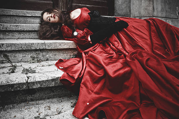 Lying and bleeding woman in a red Victorian dress stock photo
