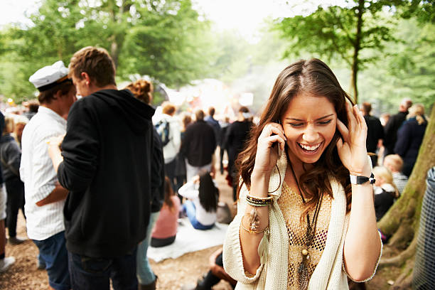 I'm at the stage area! A young woman struggling to hear on her smartphone at an outdoors festival Fingers in Ears stock pictures, royalty-free photos & images
