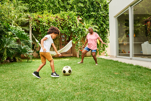 Shot of a little boy playing football with his grandmother in backyard