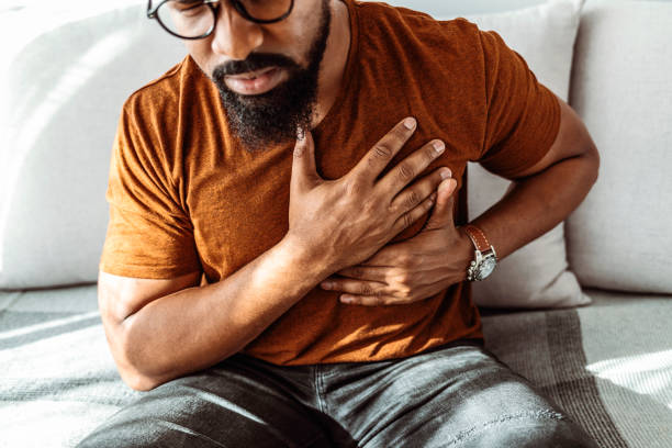 I'm having a little trouble breathing Shot of an African-American man holding his chest in pain indoors. chest pain stock pictures, royalty-free photos & images