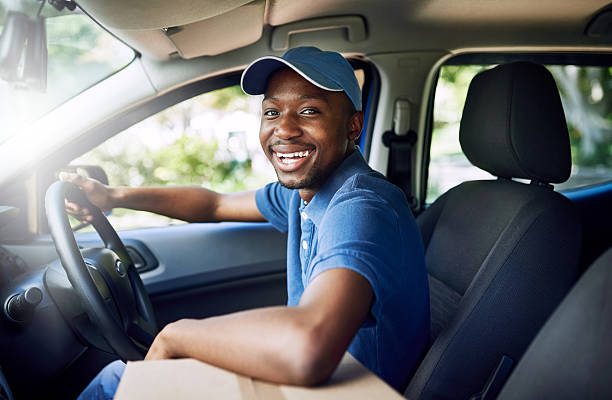 I'm on my way Portrait of a young postal working sitting in his car during a delivery black delivery man stock pictures, royalty-free photos & images