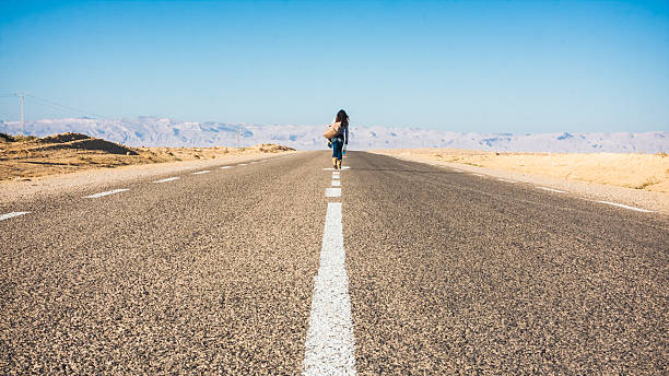 I'm Outta Here Woman walking down middle of highway with a few belongings. tunisia woman stock pictures, royalty-free photos & images