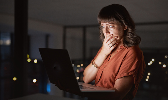 Shot of a young businesswoman looking worried while working on a laptop in an office at night