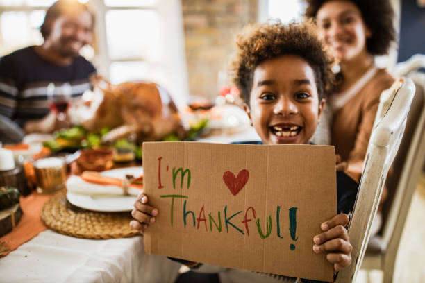 I'm thankful for this Thanksgiving day! Happy African American girl holding 'I'm thankful' sign and looking at camera during Thanksgiving meal with her parents. thanksgiving stock pictures, royalty-free photos & images