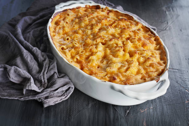 Macaroni and Cheese High angle view of a dish of fresh baked macaroni and cheese with table cloth and old wood spoon over a rustic dark background. casserole dish stock pictures, royalty-free photos & images