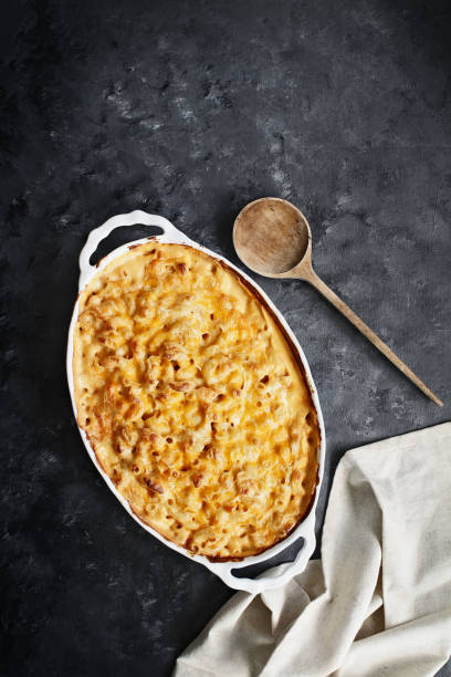 Macaroni and Cheese High angel view of a dish of fresh baked macaroni and cheese with table cloth and old wood spoon over a rustic dark background. gratin stock pictures, royalty-free photos & images