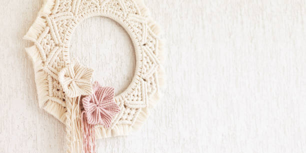 Macrame wreath with cotton flowers on a white decorative plaster wall. Natural cotton thread and rope. Eco decor for home. Creative woman hobby. Copy space. Banner stock photo