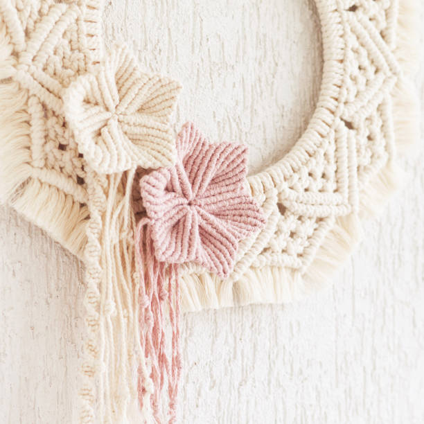 Macrame wreath with cotton flowers on a white decorative plaster wall. Natural cotton thread and rope. Eco decor for home. Creative woman hobby. Copy space stock photo