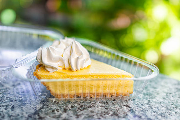 Macro closeup of one individual serving size of key lime pie cake with whipped cream in plastic container on table at cafe restaurant bakery in Key West, Florida by outdoor garden stock photo