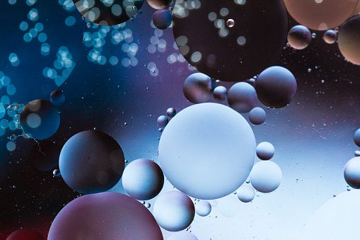 Close up macro image depicting droplets of oil in water on a multi colored background. The oil forms interesting circles and spheres in the water, and colorful background produces and abstract effect. Horizontal color image with copy space.