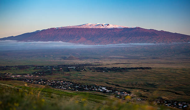 Magnificent and Snow Capped Mauna Kea Looms over the Landscape The beautiful and nearly 14,000 foot tall Hawaiian Volcano—Mauna Kea—looms over the landscape on the Big Island of Hawaii. Rolling hills in the foreground give way to vast countryside. Hawaii's tallest volcano is snow capped and rises well above the thin cloud layer. mauna kea stock pictures, royalty-free photos & images
