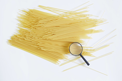 Magnifying glass and quality durum wheat spaghetti on a white background. Concept of analysis and examination of the quality of flour products. Consumerism. Inspection products before sale. Daylight